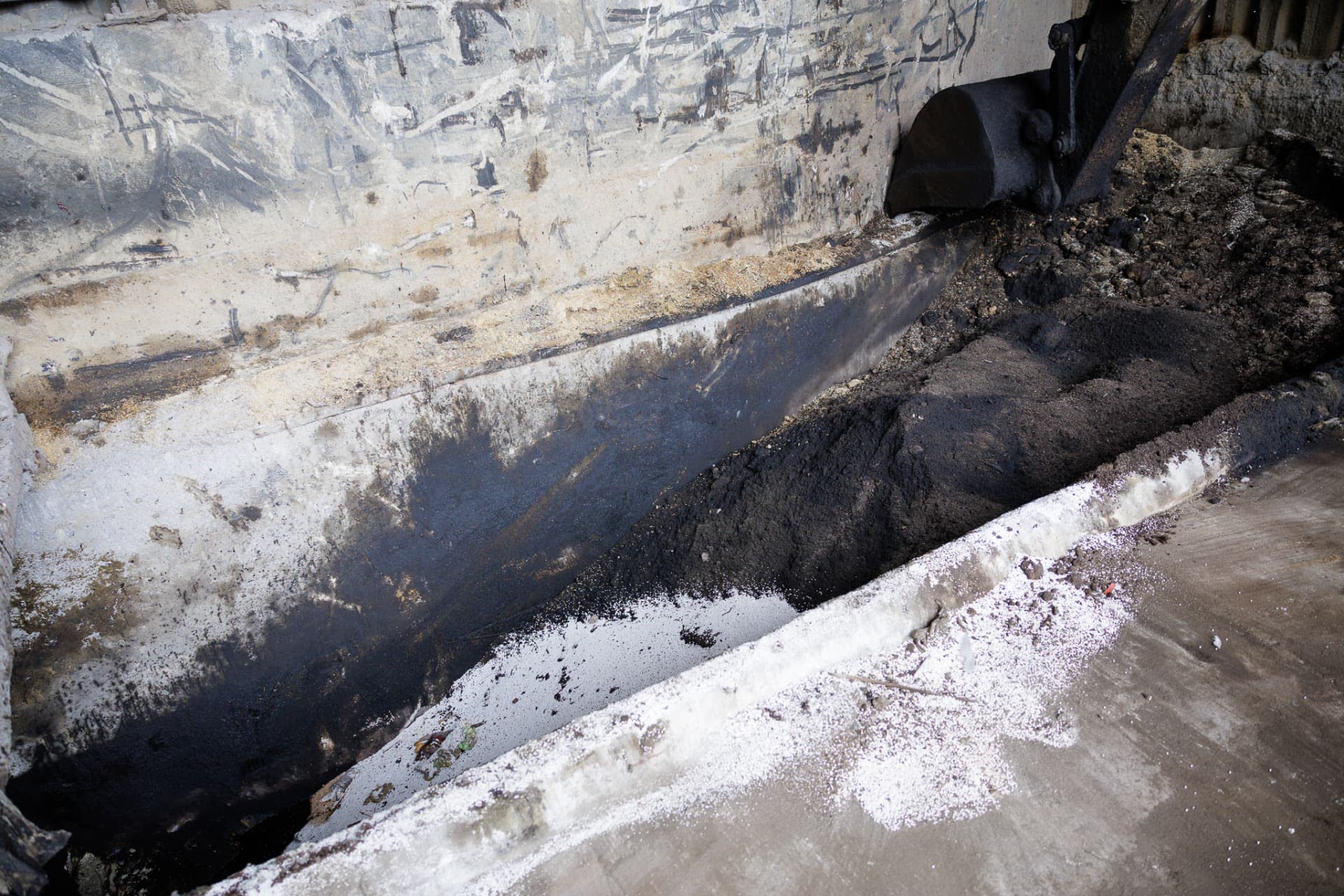 Excavator bucket handling contaminated soil in a lined treatment pit